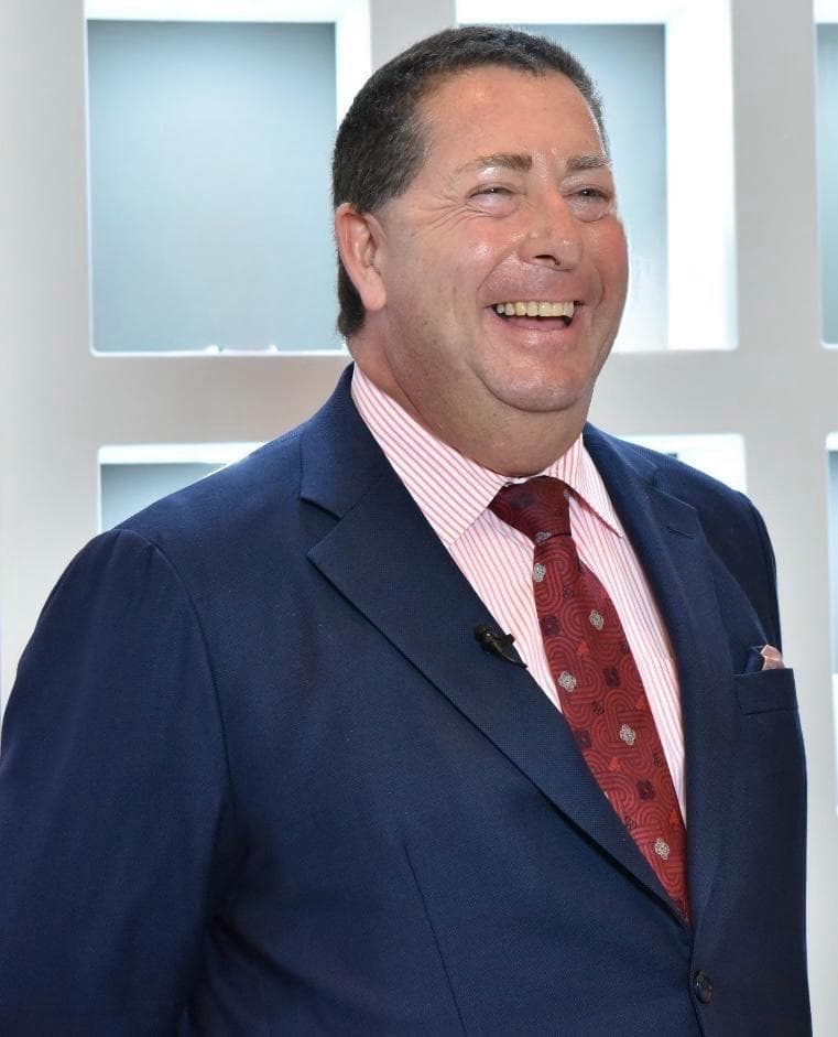 Smiling man wearing a navy blue suit, pink striped shirt, and red patterned tie.